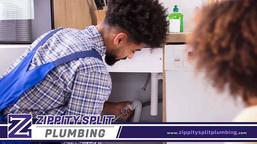 Woman Looking At Male Plumber Cleaning Clogged Pipes