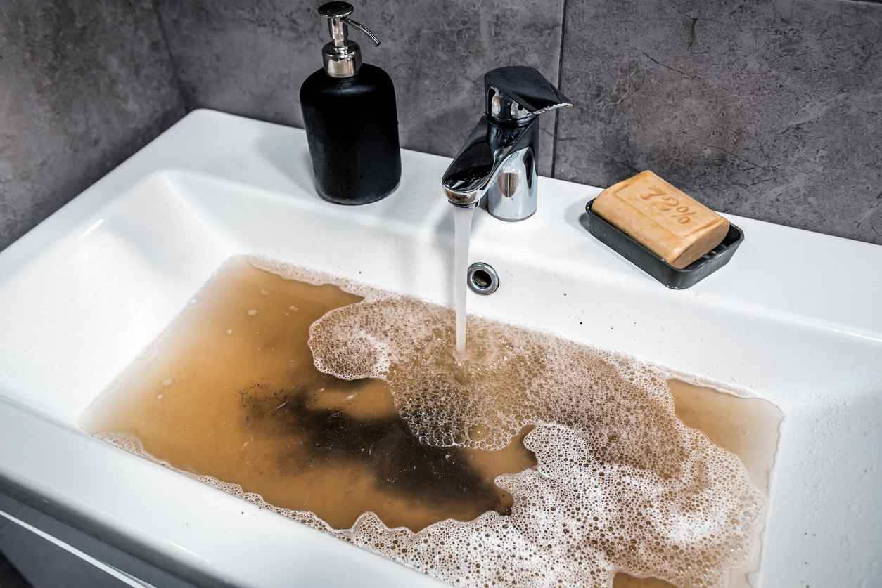Clogged sink in bathroom, sink with dirty water, brown soap. Plumbing problems.