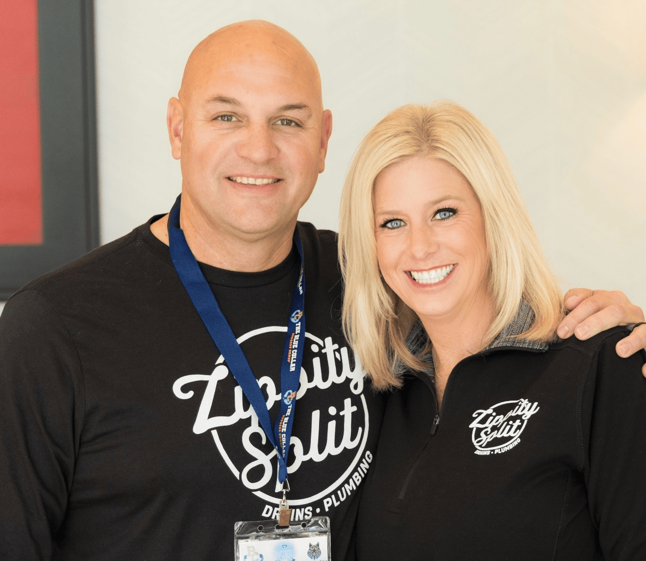 Two smiling coworkers pose together in matching black shirts with the 'Livity Split' logo; man on the left wears a blue lanyard and badge, woman on the right has blonde hair and smiles at the camera.