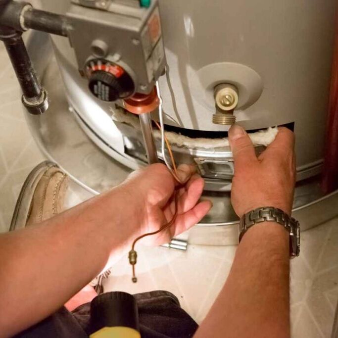A man uses a flashlight to help him see the hot water heater in a dark closet